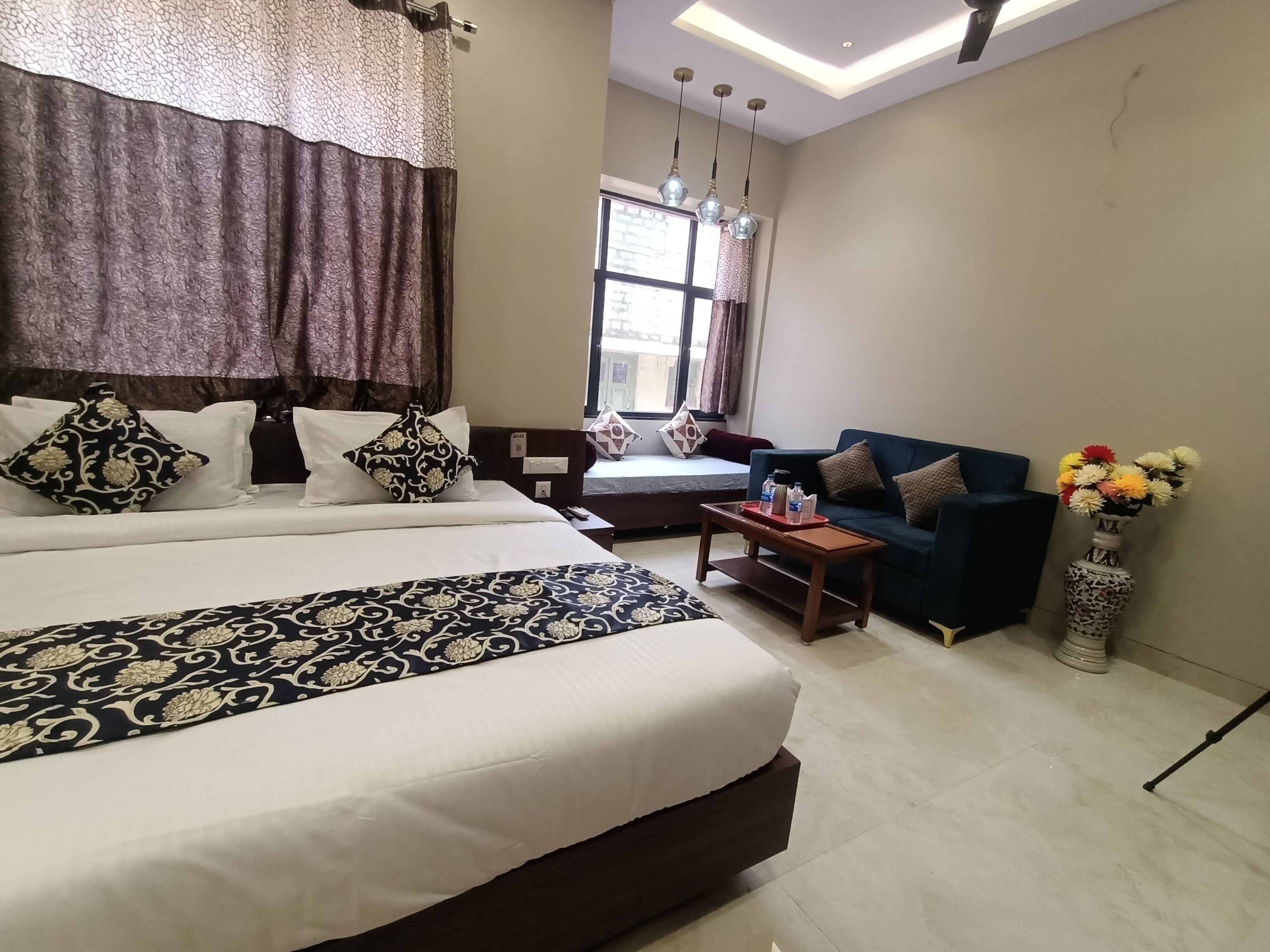 A hotel room with a large bed, a sofa, a small table, and a vase of flowers.