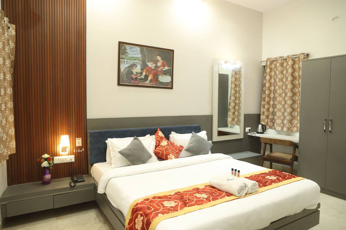 A hotel room with a bed, bedside table, lamp, and a painting on the wall.