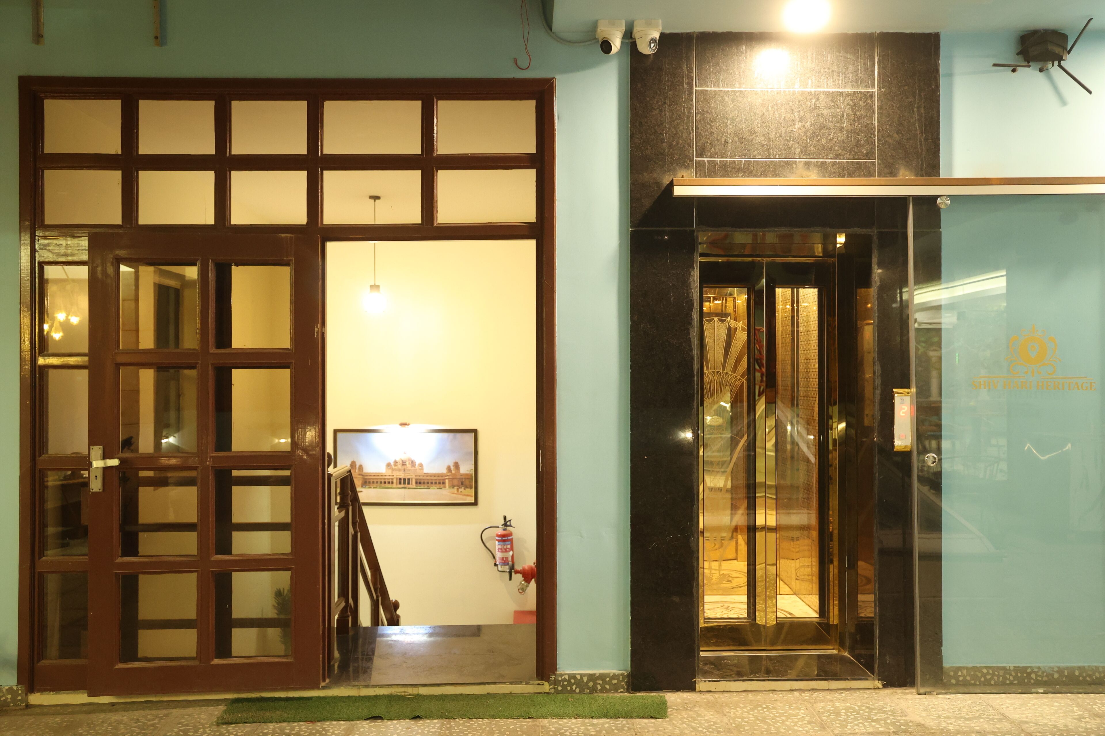 Entrada de hotel con puerta de madera, una escalera y puerta de cristal que da al interior.