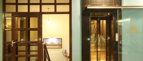 Entrada de hotel con puerta de madera, una escalera y puerta de cristal que da al interior.