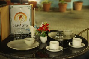 Une table dressée pour le dîner, avec un menu intitulé « La Cuillère d’or » et une plante en pot ornée de fleurs rouges.