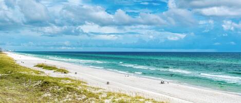 A beach with white sand, ocean waves, and a clear sky.