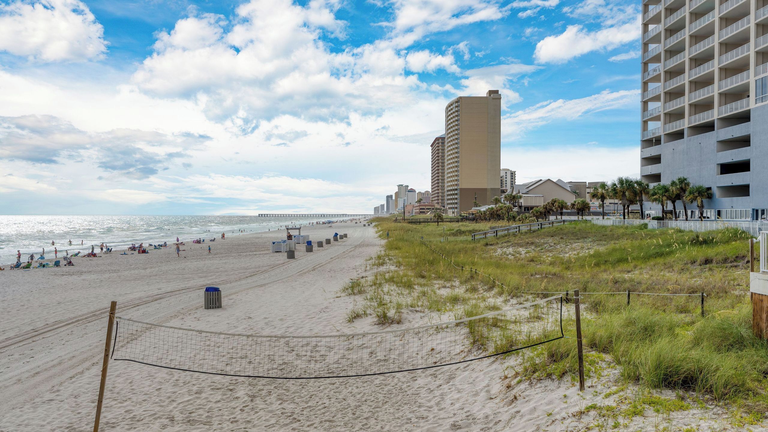 A beach with a high-rise building, a pier, and a fence.