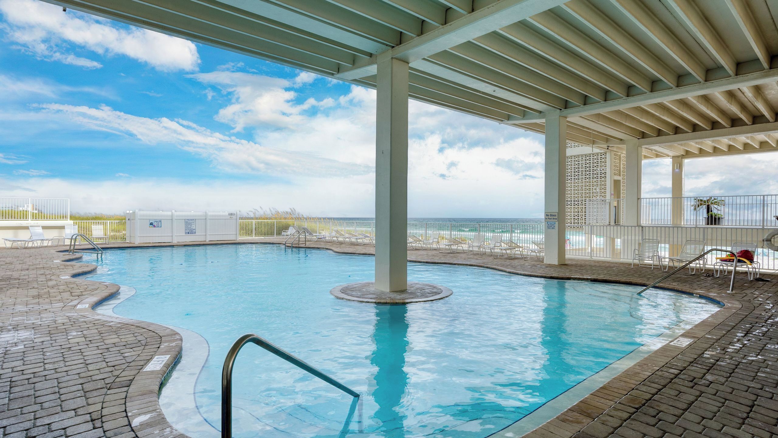 Ein Pool mit Meerblick, ein überdachter Bereich mit Stühlen und ein klarer Himmel.
