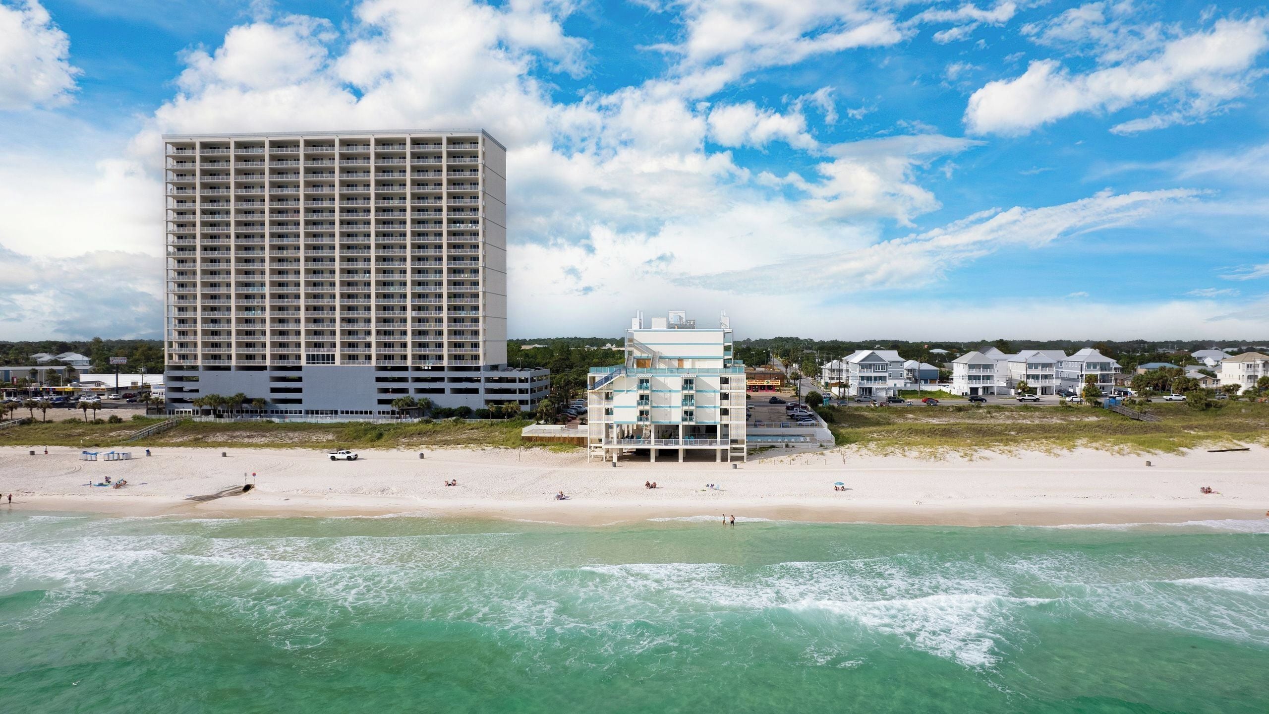 Un hôtel en bord de mer, avec plusieurs étages, une plage au premier plan et un ciel dégagé.