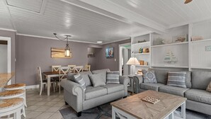 Una sala de estar con un sofá gris, una mesa de centro de madera y un comedor con mesa y sillas.