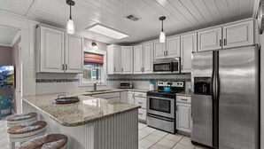 Una cocina moderna con armarios blancos, electrodomésticos de acero inoxidable, encimera de granito y una isla grande con taburetes.