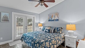 Un dormitorio con cama, dos mesitas de noche, ventilador de techo y obras de arte en las paredes.