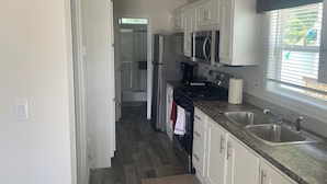 A modern kitchen with white cabinetry, stainless steel appliances, and a window with blinds. - Cherokee Lake Cozy Cabin in Cherokee Landing (Lakeview)