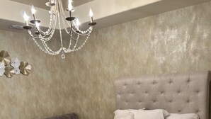 A bedroom with a large bed, a tufted headboard, a dark-colored sofa, and a chandelier.