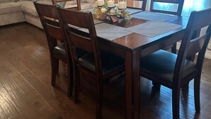 A dining area with a wooden table, four chairs, and a chandelier.