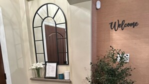 A hallway with a welcome sign, a potted plant, a framed menu, and a window with a metal grille.