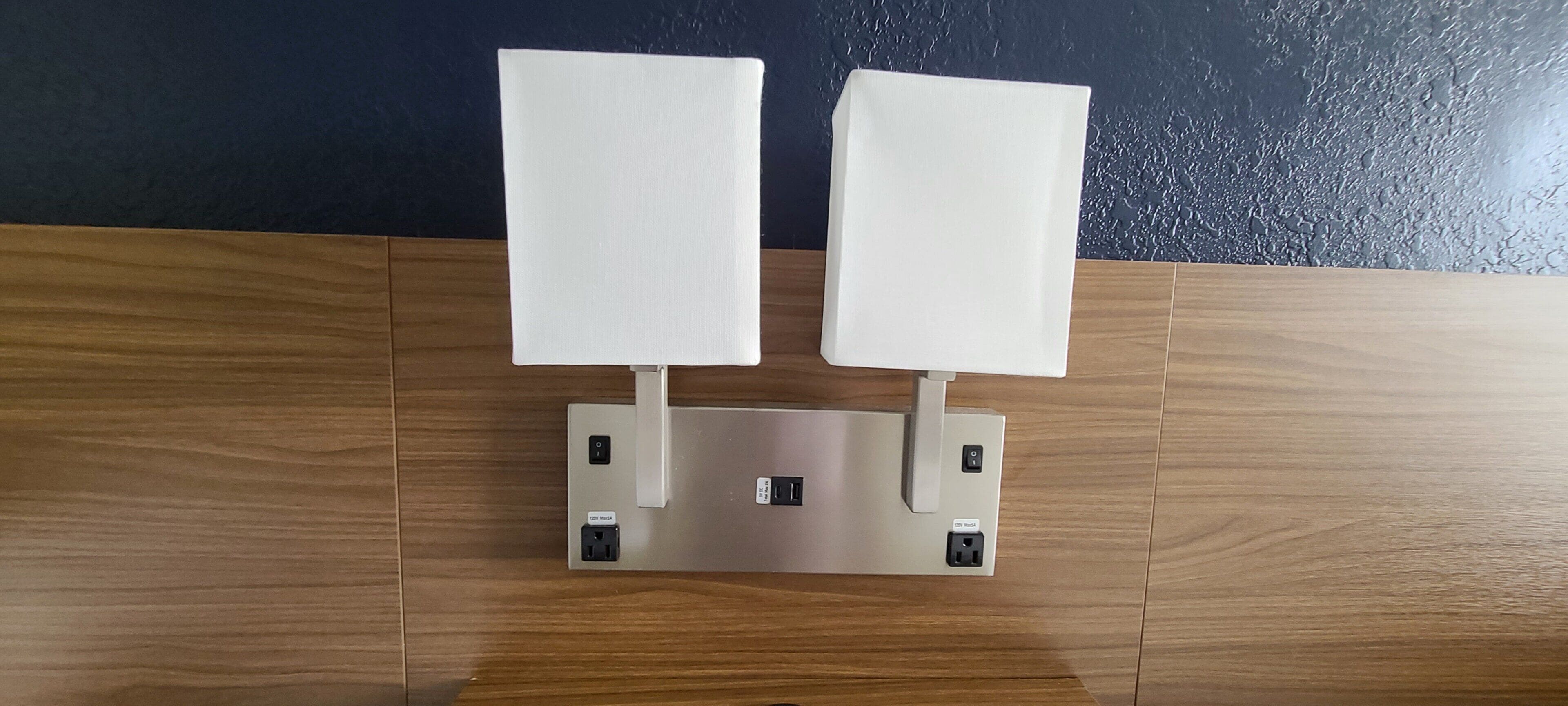 A wall-mounted light fixture with two rectangular light panels on a wooden floor against a dark wall.