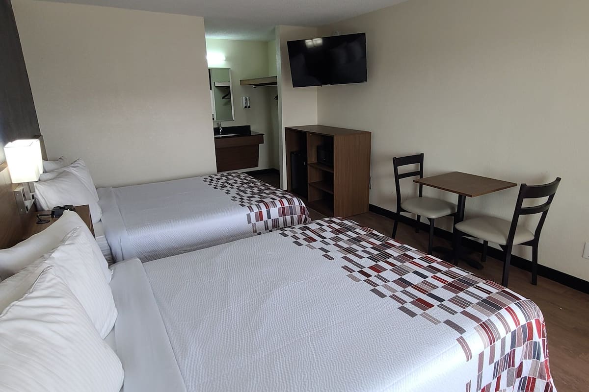 A hotel room with two beds, a desk, a chair, a TV, and a bathroom in the background.