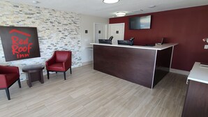 A reception area with a modern design, featuring a reception desk, two red chairs, a small table, and a wall-mounted sign. - Red Roof Inn Byron (Byron)