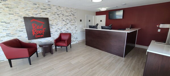 A reception area with a modern design, featuring a reception desk, two red chairs, a small table, and a wall-mounted sign. - Red Roof Inn Byron (Byron)