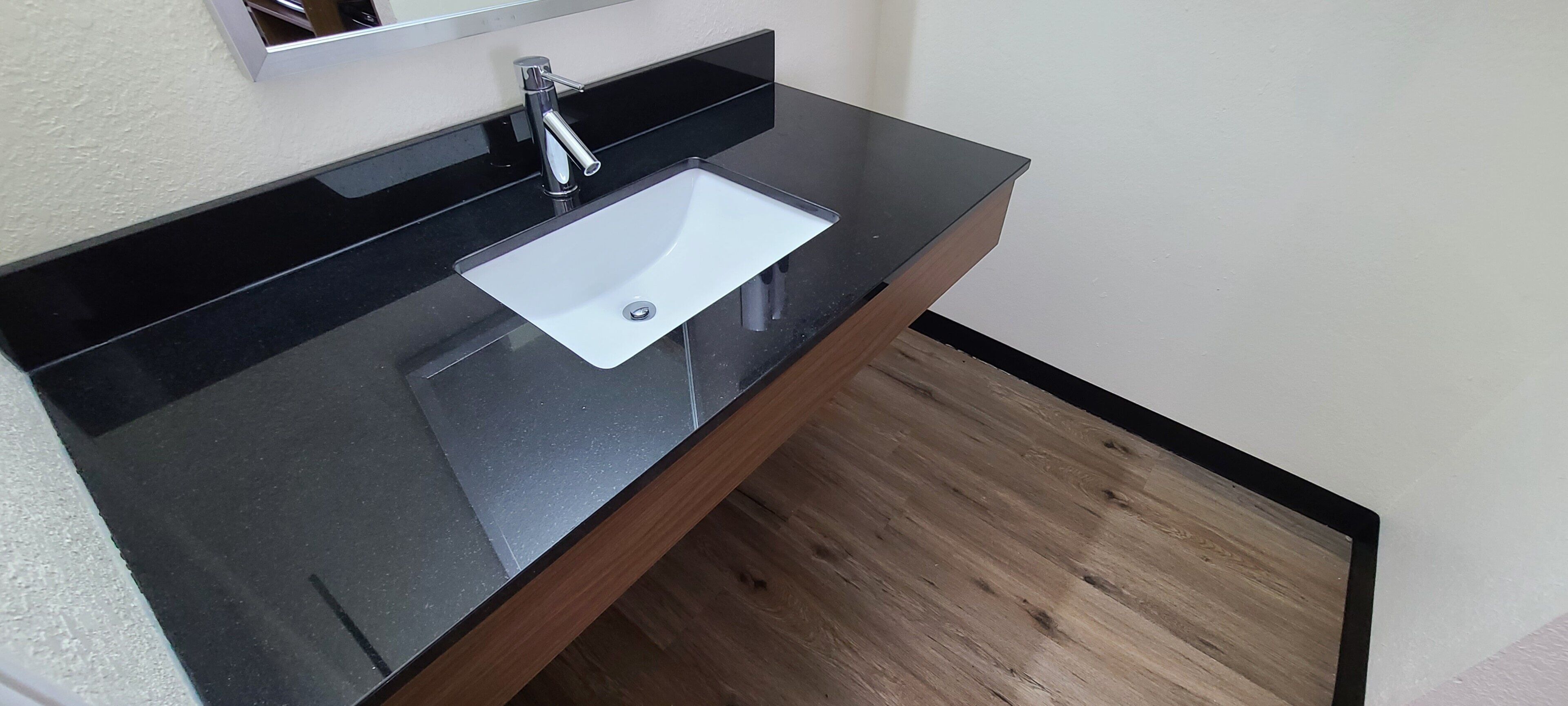 A bathroom with a black countertop, a white sink, and a wooden floor.