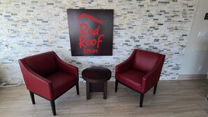 Une pièce avec deux chaises rouges, une petite table ronde et une enseigne « Red Roof Inn » accrochée au mur.