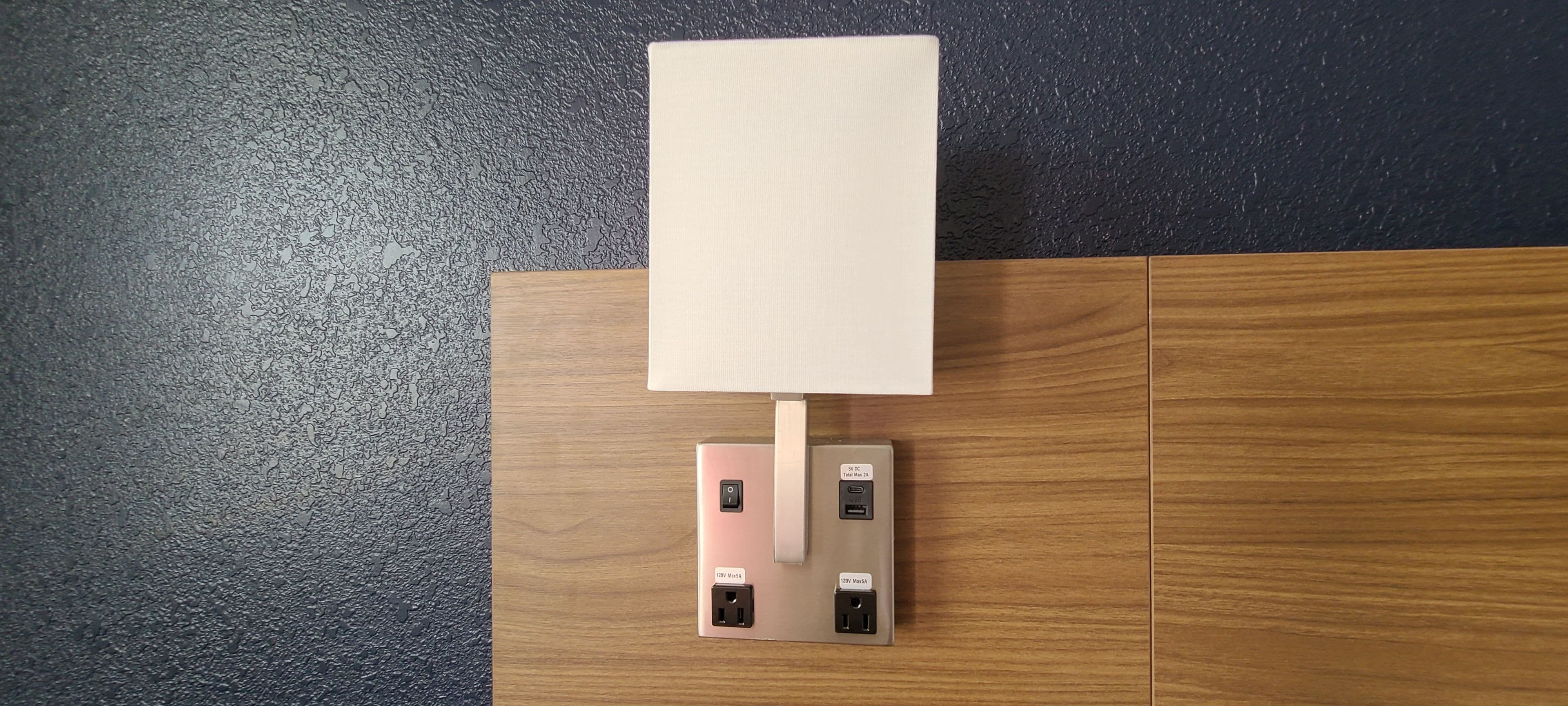 A wall-mounted lamp with a rectangular shade, a power outlet, and a USB port on a wooden panel.