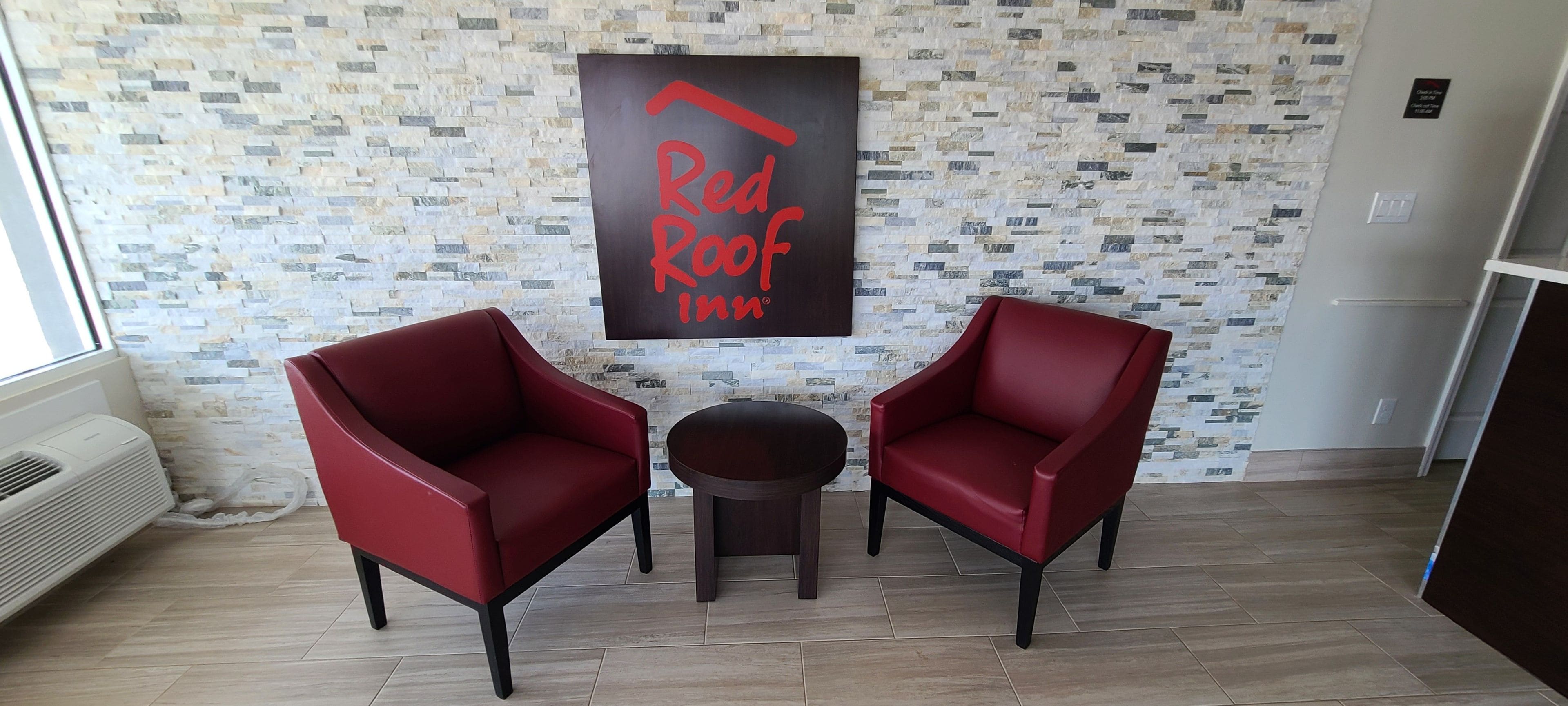A room with two red chairs, a small round table, and a 'Red Roof Inn' sign on the wall.