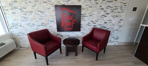 A room with two red chairs, a small round table, and a 'Red Roof Inn' sign on the wall. - Red Roof Inn Byron (Byron)