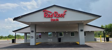 Un Red Roof Inn con techo plano, zona de estacionamiento techada y cielo despejado.