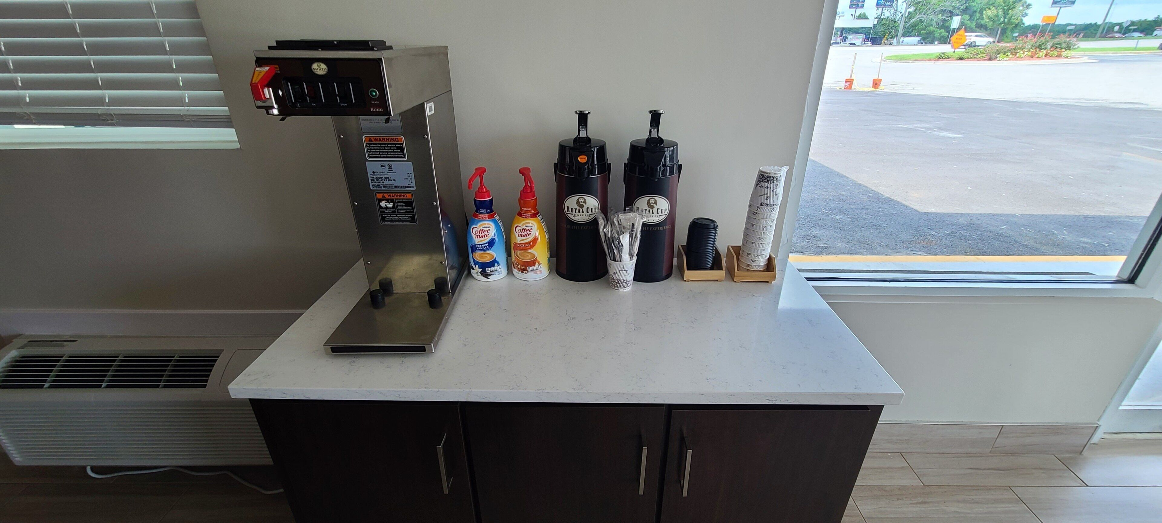 A coffee station with a coffee machine, two coffee makers, and condiments.