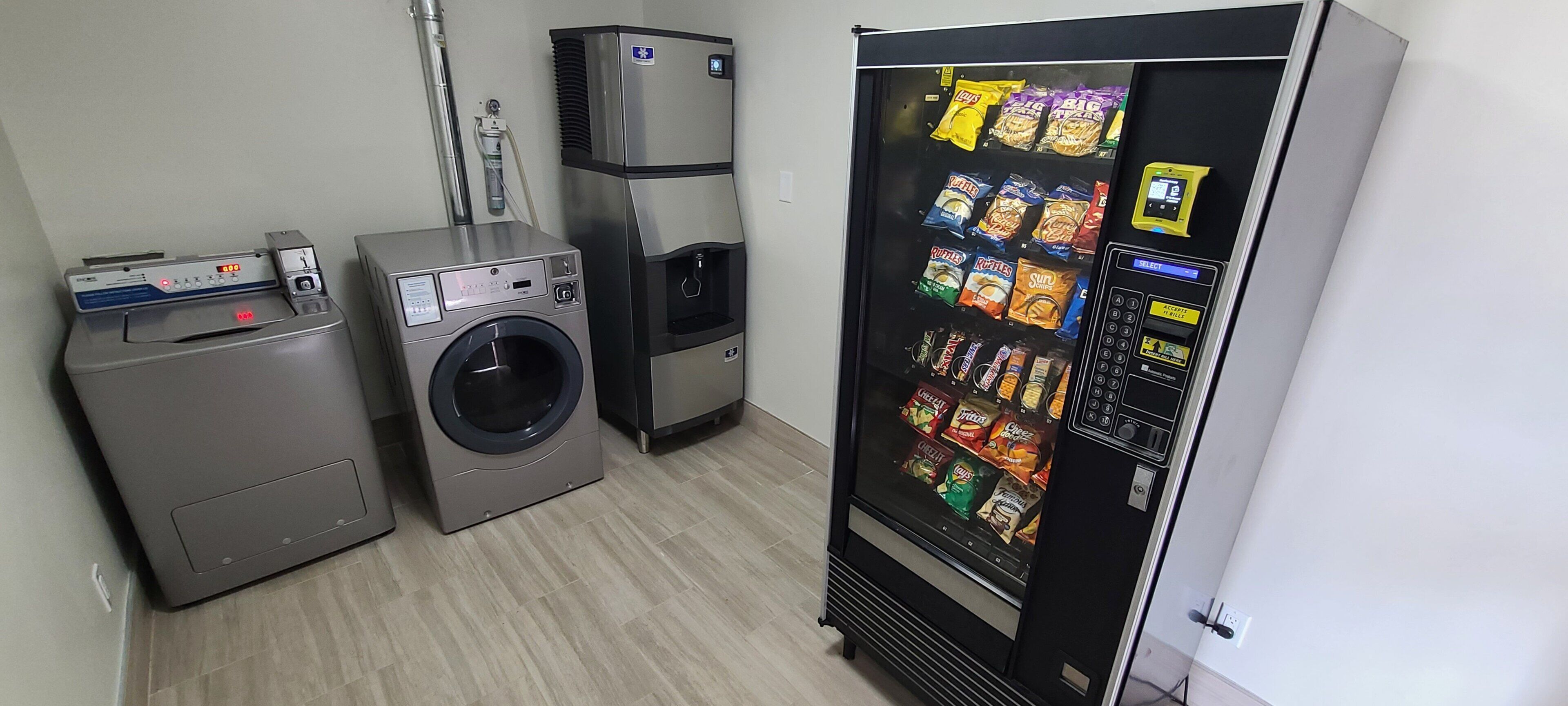 A laundry room with a washing machine, dryer, and a vending machine stocked with snacks.