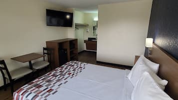 A hotel room with a bed, a desk, a chair, a television, and a small kitchenette.