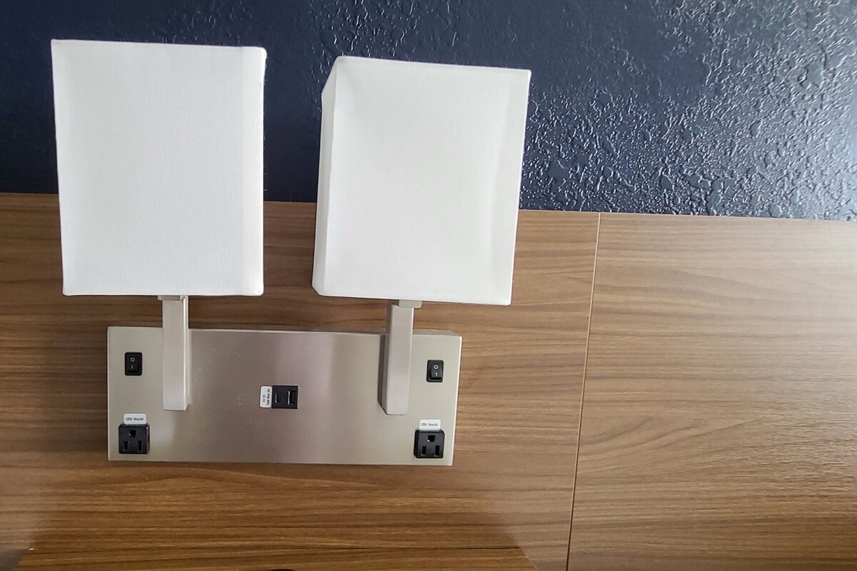 A wall-mounted light fixture with two rectangular light panels on a wooden floor against a dark wall.