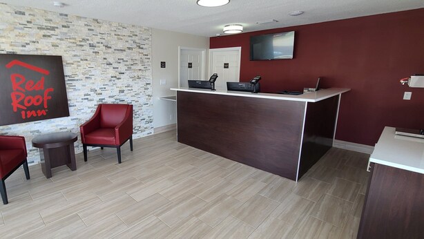 Un espace d’accueil au design moderne, comprenant un comptoir de réception, deux chaises rouges, une petite table et un panneau fixé au mur.