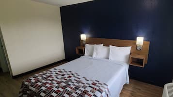 Una habitación de hotel con una cama, dos lámparas de noche, un cabecero de madera y un ventanal con persianas.