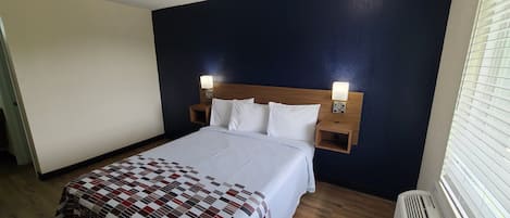 A hotel room with a bed, two bedside lamps, a wooden headboard, and a window with blinds.