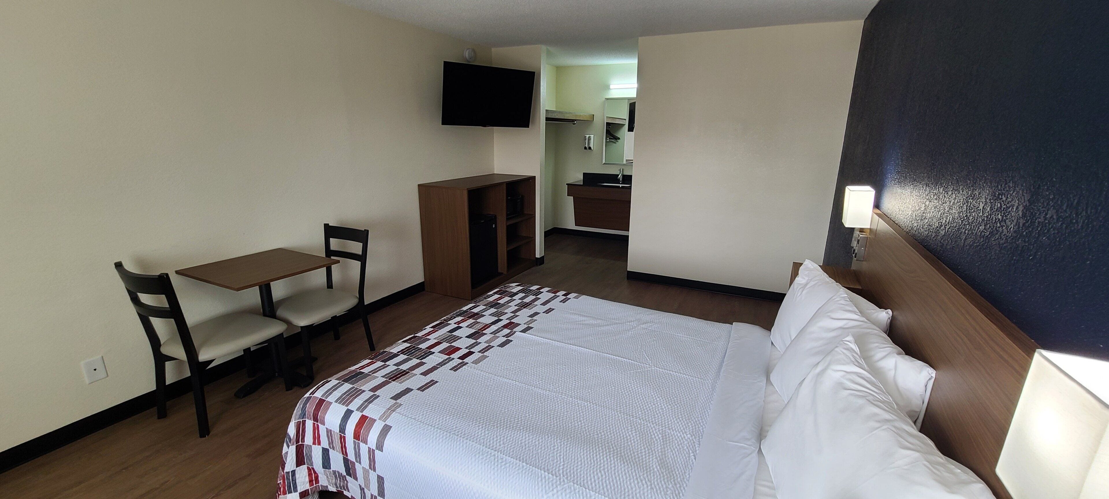 Une chambre d’hôtel avec un lit, un bureau, une chaise, une télévision et une salle de bain visible à travers une porte ouverte.