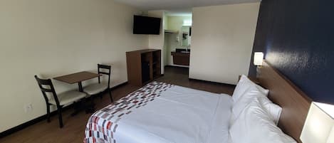 Une chambre d’hôtel avec un lit, un bureau, une chaise, une télévision et une salle de bain visible à travers une porte ouverte.