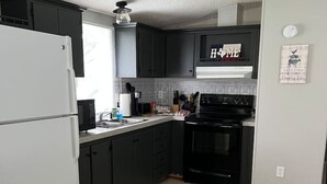 A compact kitchen with dark cabinets, a white refrigerator, a black stove, and a window with blinds. - Casita on the Ranch-wildlife,sunsets, stars, relax (Spring Branch)