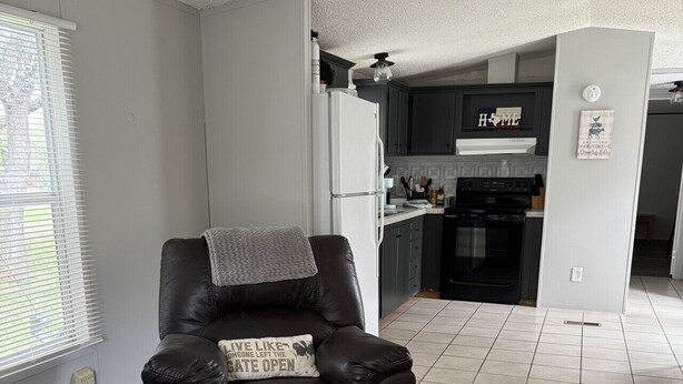 A modern living room with a leather recliner, a kitchen in the background, and a grey tiled floor. - Casita on the Ranch-wildlife,sunsets, stars, relax (Spring Branch)