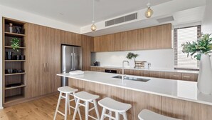 Une cuisine moderne dotée d’un grand îlot central, de tabourets de bar, de meubles en bois et d’un réfrigérateur encastré.