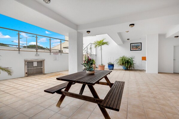 A spacious patio with a wooden table and benches, surrounded by potted plants and a view of the sky. - Perfect Family Base for the Reef | Walk to Esplanade & Lagoon | Portofino (Cairns City)