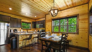 A wooden cabin interior with a kitchen, dining area, and large windows. - Mountain Magic: The Perfect Romantic Cabin Getaway (Gatlinburg)