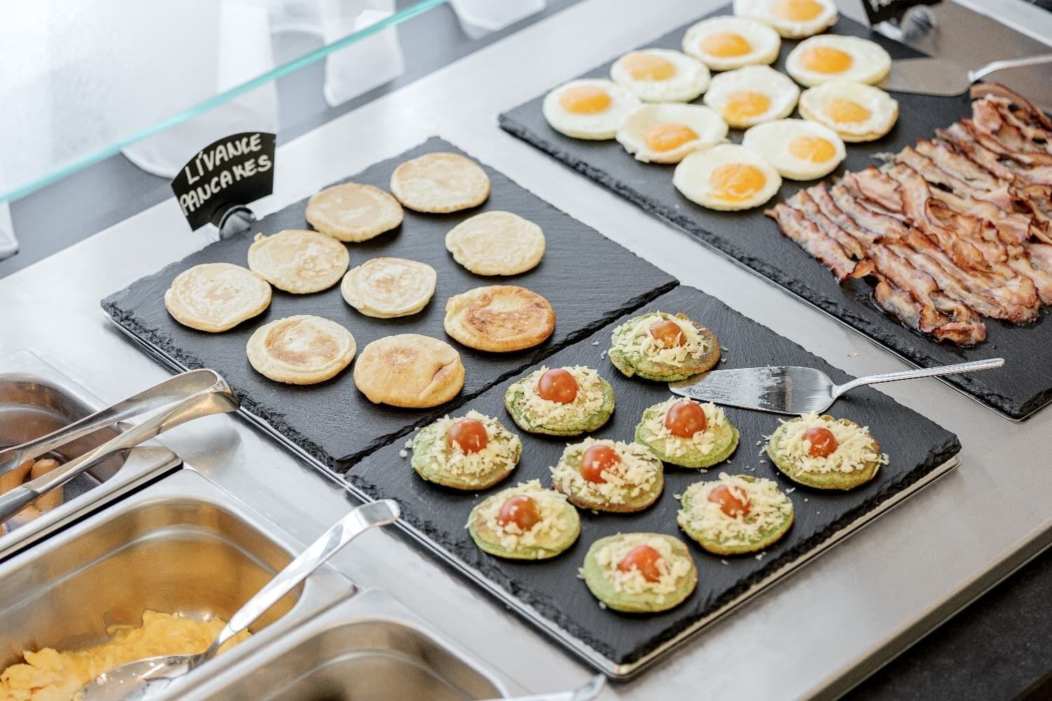 Un bufé con diversas opciones de comida, como huevos, tocino y sándwiches abiertos.