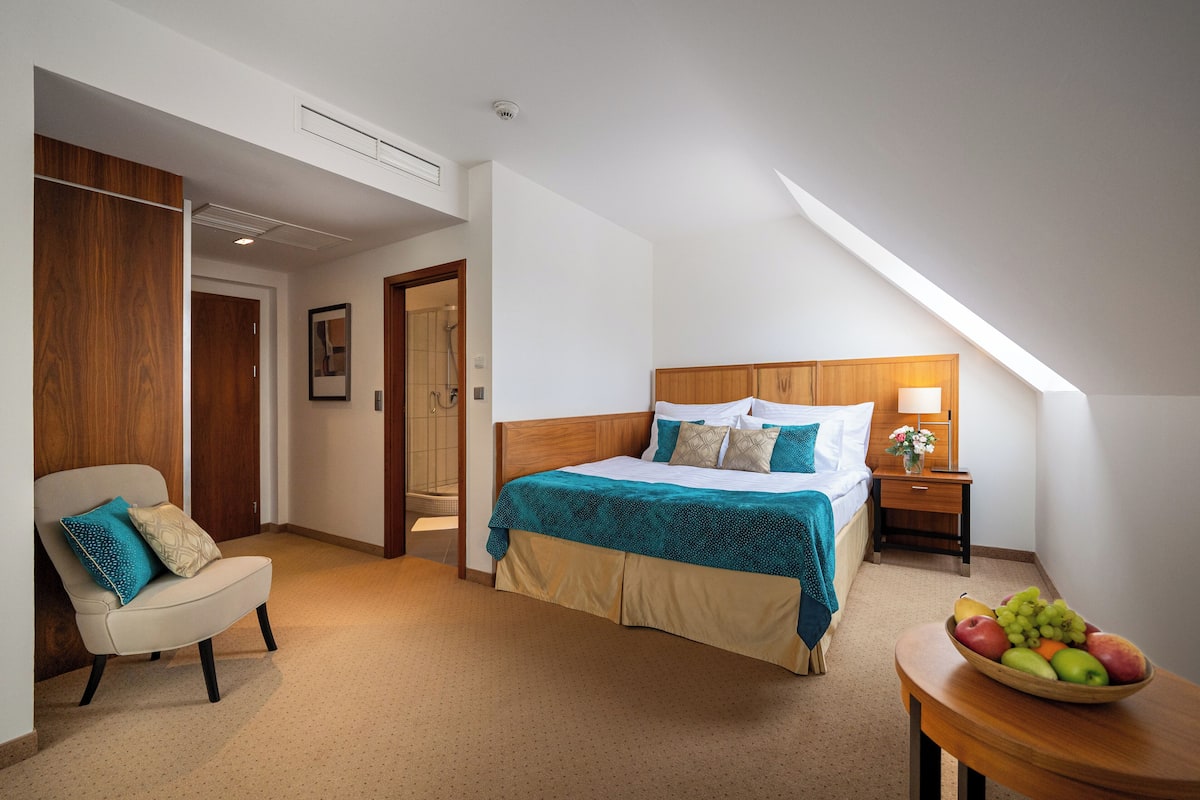 A bedroom with a bed, a chair, a bedside table with a lamp, and a fruit bowl.