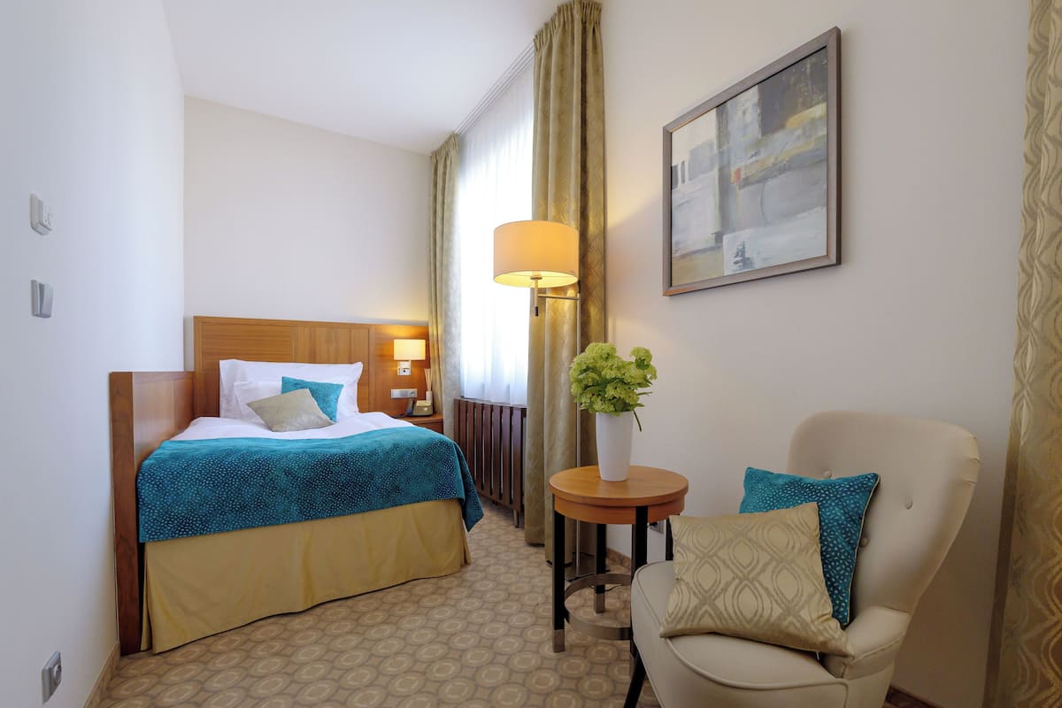 A hotel room with a bed, a chair, a lamp, and a painting on the wall.