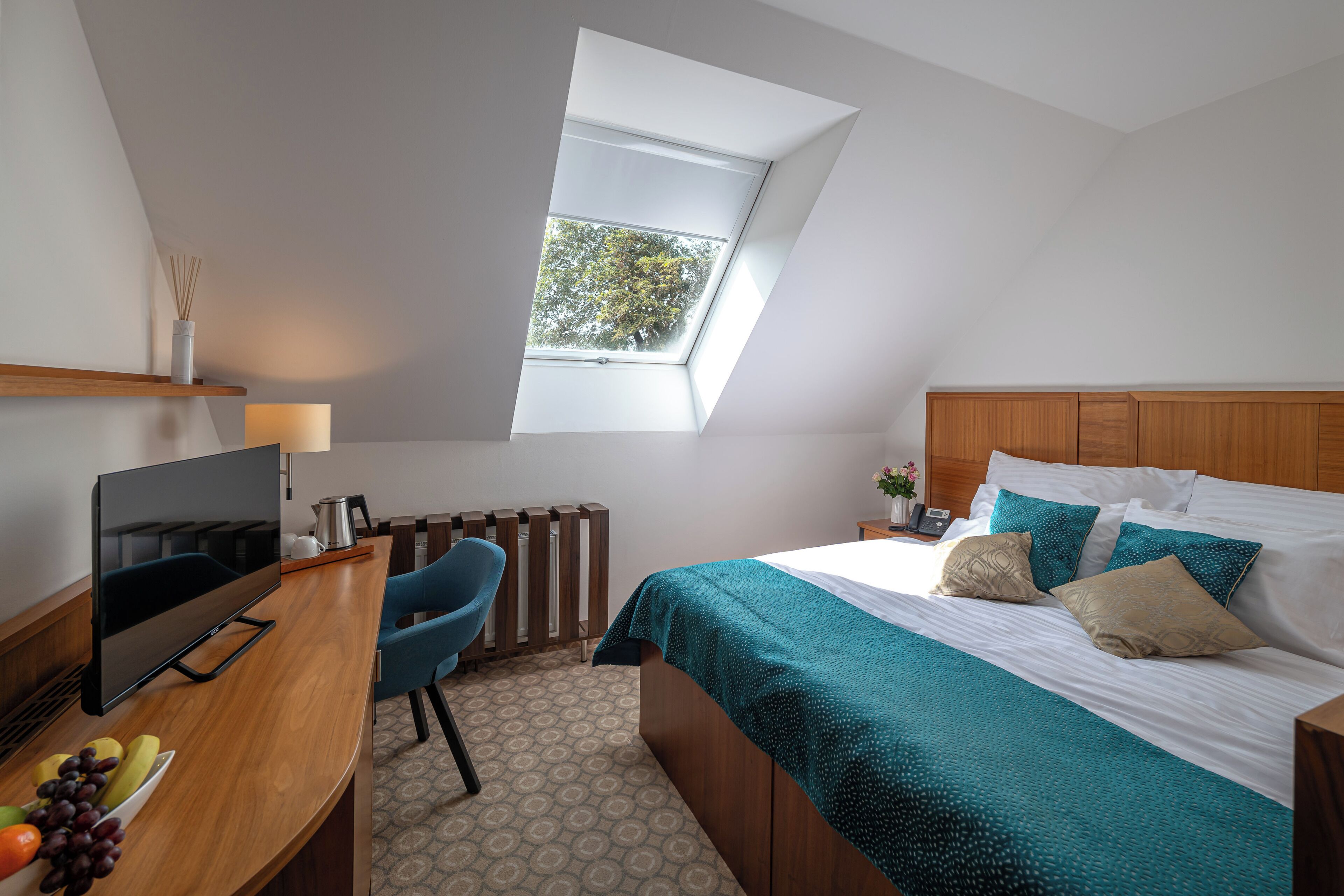 Un dormitorio con cama, escritorio con televisor, silla, ventana y radiador.