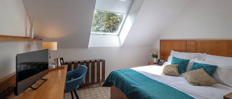 Un dormitorio con cama, escritorio con televisor, silla, ventana y radiador.