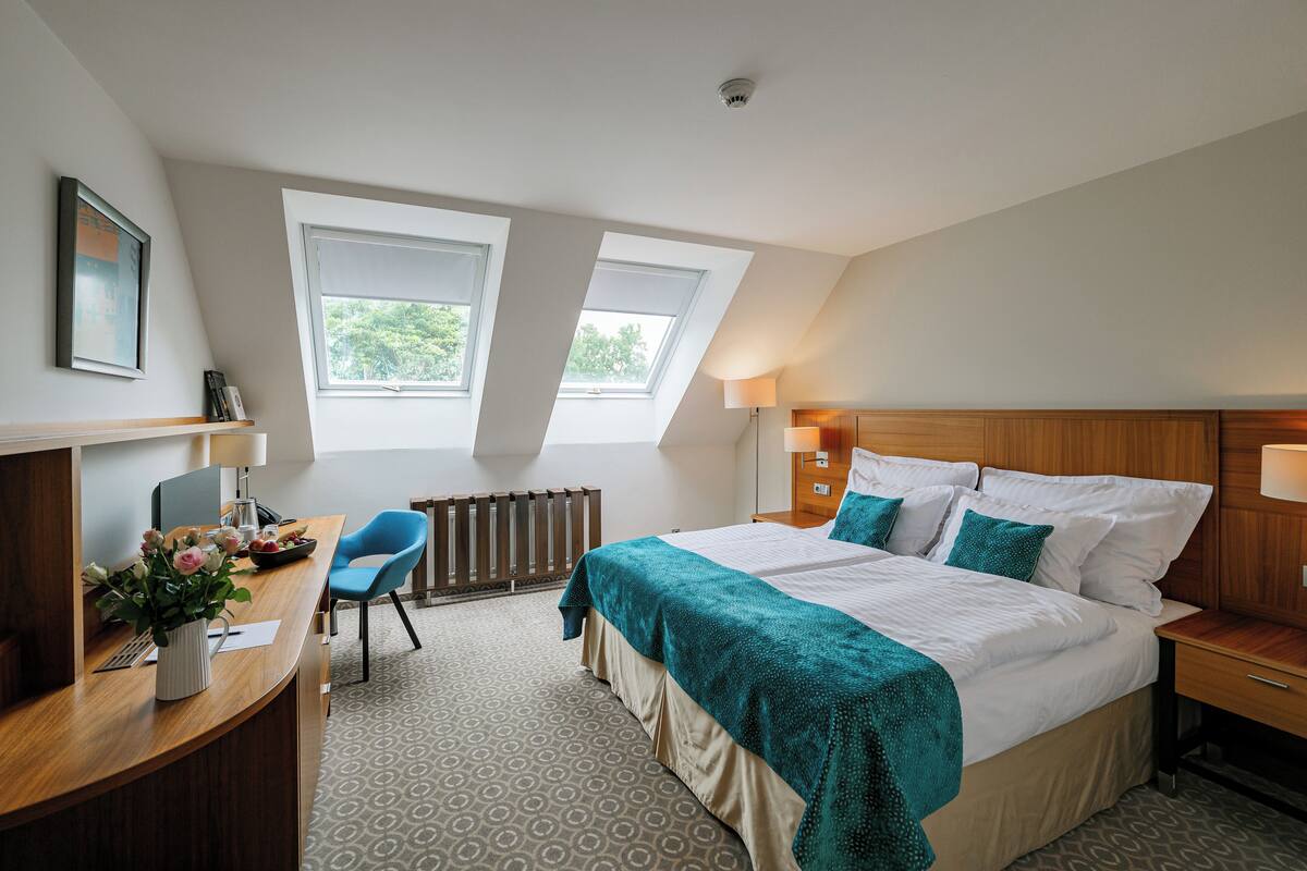 A bedroom with a bed, a desk, a chair, and two windows.