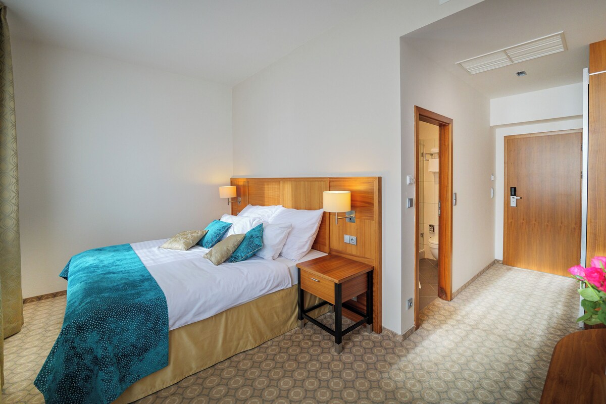 A hotel room with a bed, bedside tables, a wooden headboard, and a door.
