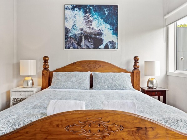 A neatly made bed with a wooden headboard, two bedside tables with lamps, a framed picture on the wall, and a window with a view of greenery. - Infine' - Infine' @ last time to relax and unwind (Augusta)