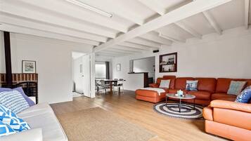 A spacious living room with a large orange sofa, a white couch, and a dining area with a table and chairs.