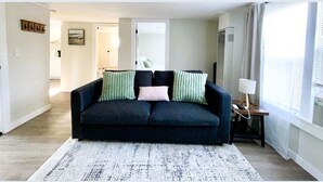 Un salon avec un canapé de couleur foncée, un tapis à motifs et une lampe posée sur une table d’appoint.